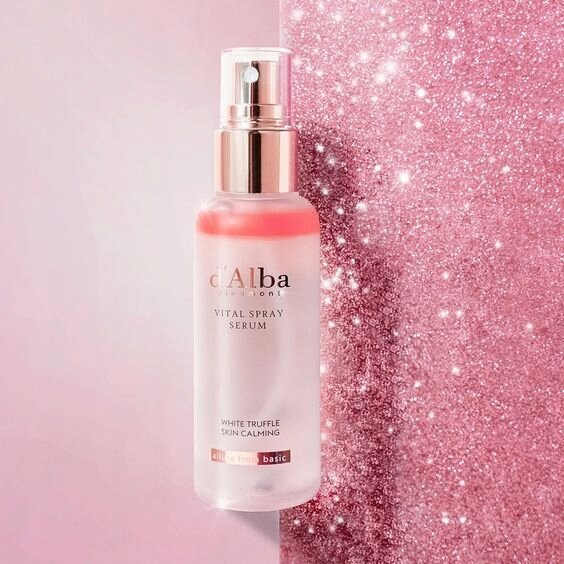 Na obrazie widoczna jest butelka z napisem \'d\'Alba Piedmont VITAL SPRAY SERUM WHITE TRUFFLE SKIN CALMING\'. Tło jest różowe i błyszczące.
