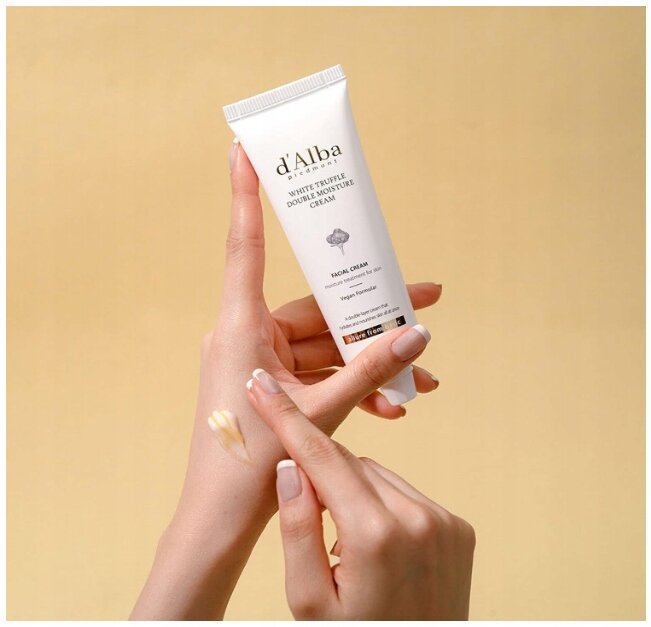 Osoba trzyma tubkę kremu d\'Alba White Truffle Double Moisture Cream i nakłada go na skórę dłoni. Tło jest jednolite, w kolorze jasnym.