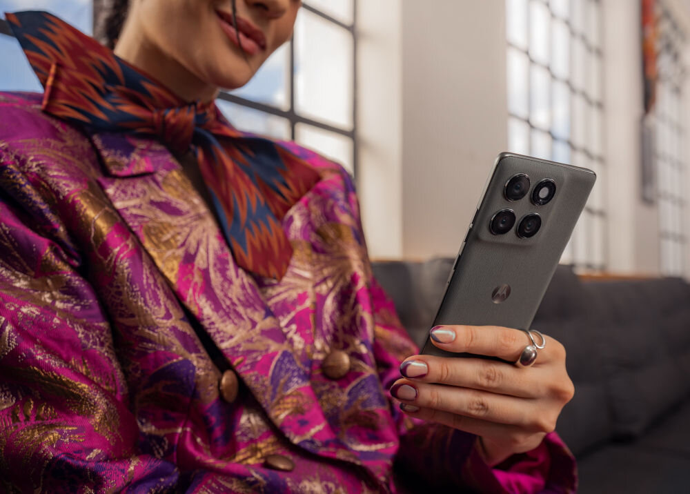 Osoba trzyma smartfon z czterema widocznymi obiektywami aparatu i logo producenta. Ubrana jest w kolorowy, wzorzysty strój.