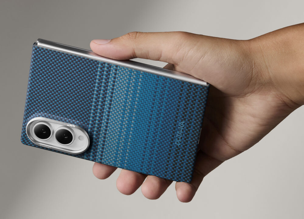 Osoba trzyma urządzenie z niebieskim etui o teksturowanej powierzchni. Na etui widoczne jest logo \'PITAKA\'.