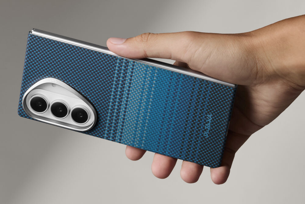 Osoba trzyma telefon w etui o niebieskim wzorze z widocznymi trzema obiektywami aparatu. Na etui znajduje się napis \'PITAKA\'.