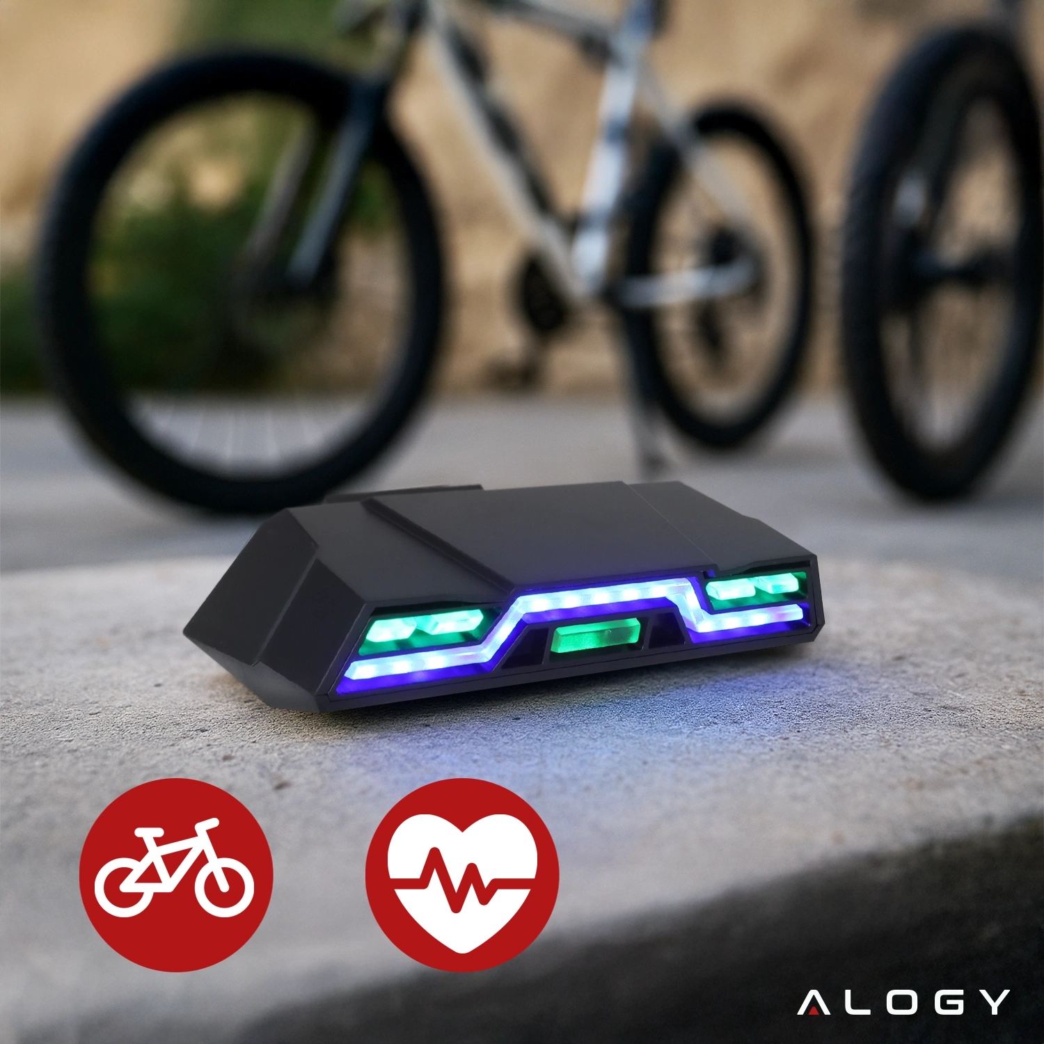 Na pierwszym planie znajduje się czarna lampka rowerowa z zielonymi i niebieskimi światłami LED. W tle widoczny jest rower, a w dolnym rogu logo \'ALOGY\'.