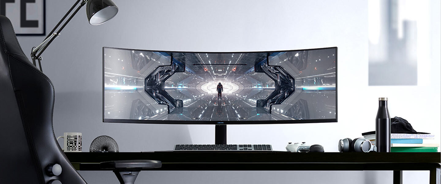 phpPbks9s przyszlosc dla graczy g9 samsung Na biurku znajduje się duży, zakrzywiony monitor z wyświetlanym futurystycznym obrazem. Obok monitora widoczne są klawiatura, mysz, słuchawki i butelka na wodę.