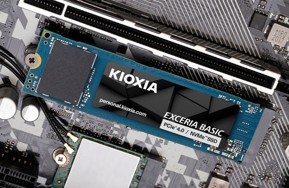 Komputer MAD DOG AURORAX-A01DR32 Zdjęcie przedstawia dysk SSD zamontowany w gnieździe na płycie głównej komputera. Niebieska płytka drukowana komponentu z widocznymi układami scalonymi jest częściowo przykryta czarną etykietą z logotypem producenta