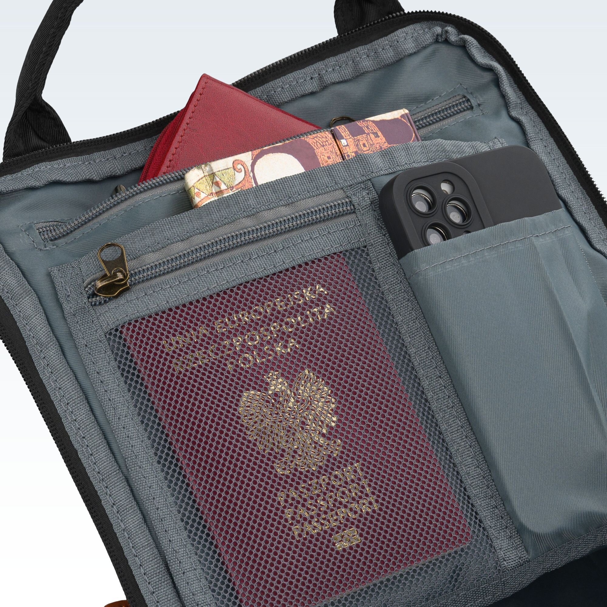 Wnętrze plecaka z widocznymi kieszeniami, w których znajdują się paszport, telefon i czerwony portfel. Paszport ma napis \'UNIA EUROPEJSKA RZECZPOSPOLITA POLSKA\'.