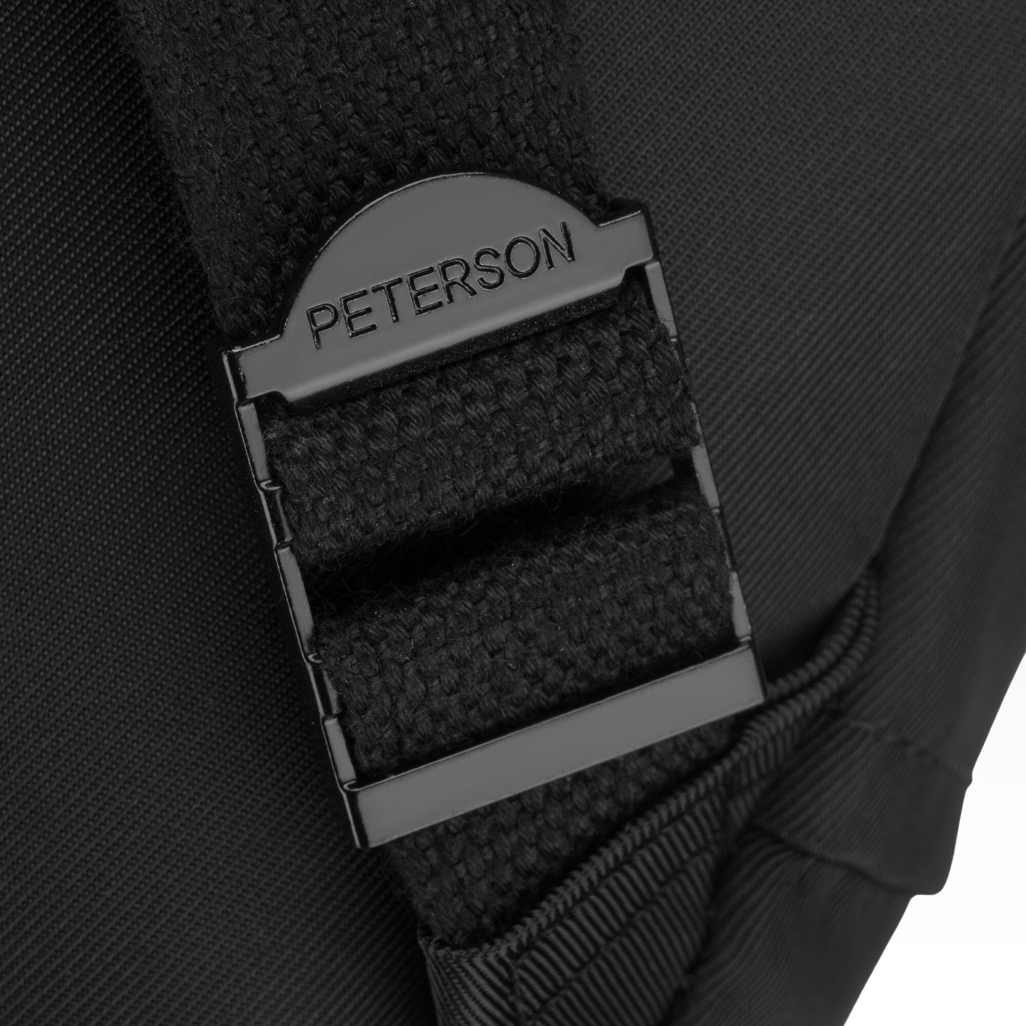 Zbliżenie na czarny pasek plecaka z plastikową klamrą, na której widnieje napis \'PETERSON\'.