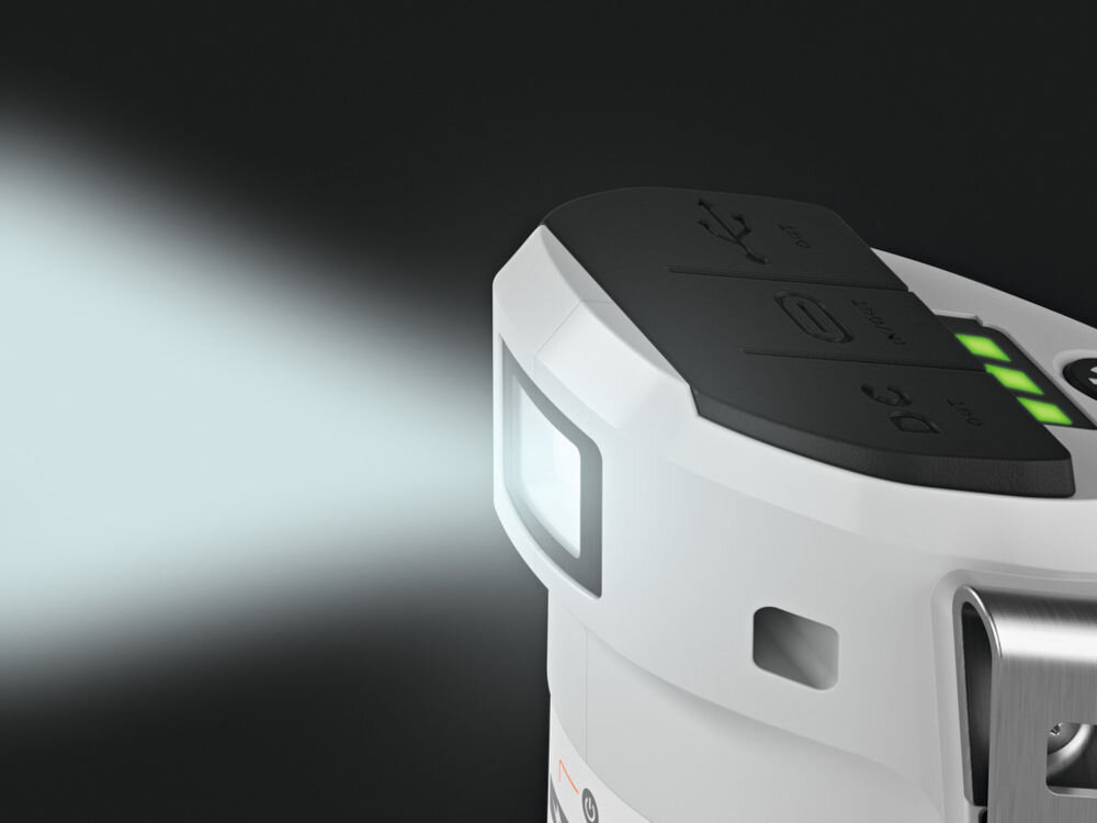 Obraz przedstawia biały powerbank z włączoną latarką, emitującą jasne światło. Na górnej części urządzenia widoczne są symbole USB i DC oraz wskaźnik naładowania z zielonymi diodami.