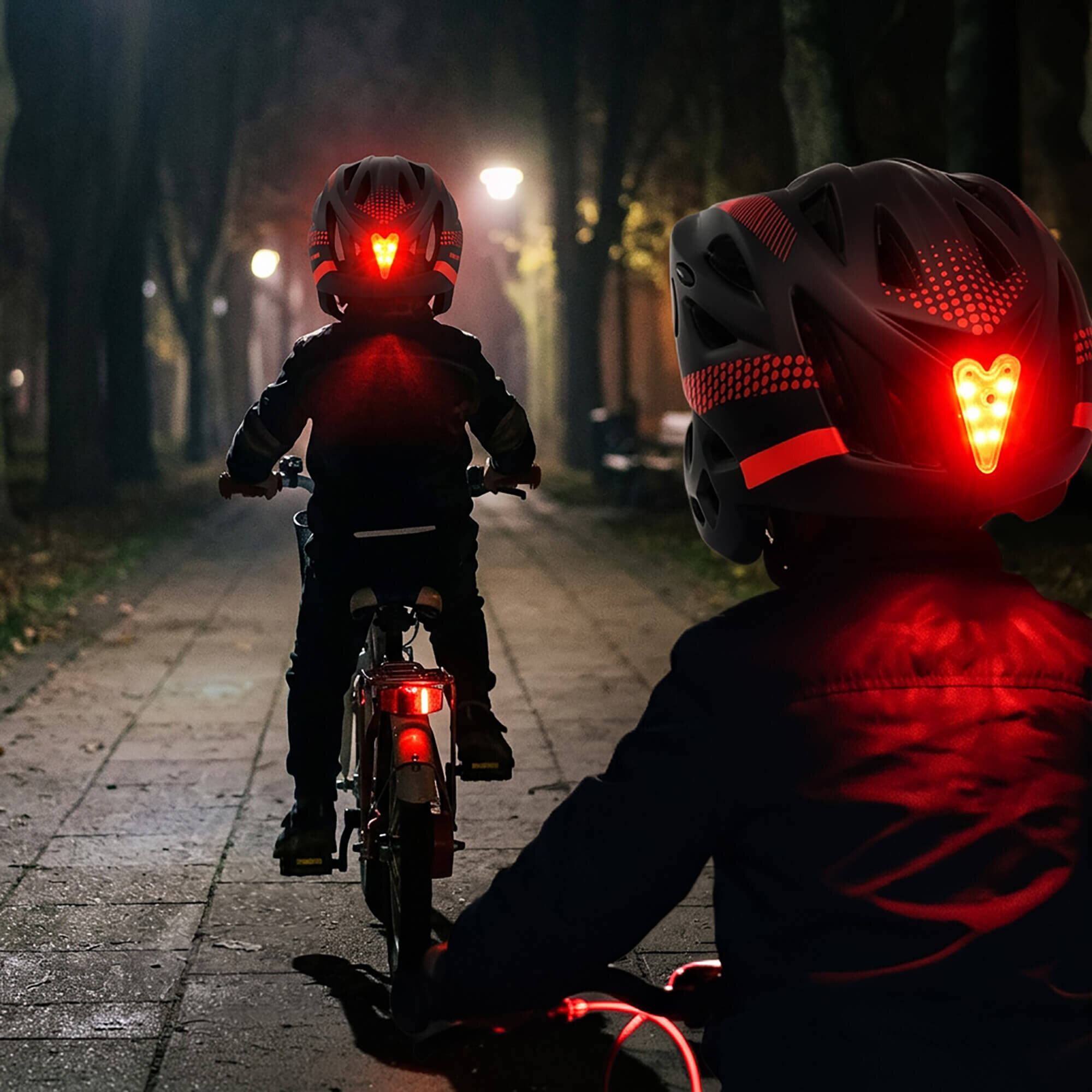Dwoje dzieci jedzie na rowerach nocą, mają na głowach kaski z czerwonymi światłami LED. Ścieżka jest oświetlona latarniami, a wokół znajdują się drzewa.