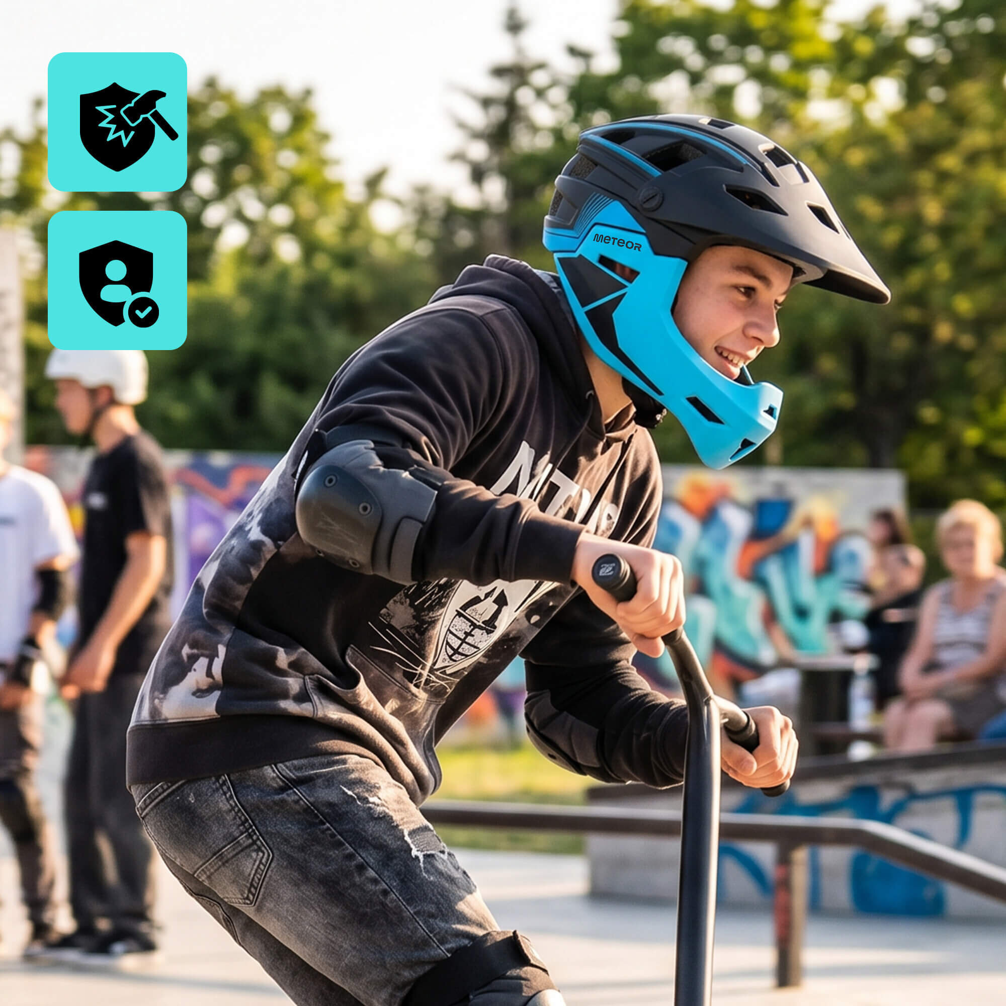 Osoba w czarno-niebieskim kasku rowerowym full-face METEOR Hydra S 51-55 cm jedzie na hulajnodze w skateparku. W tle widoczne są inne osoby oraz graffiti na murze.