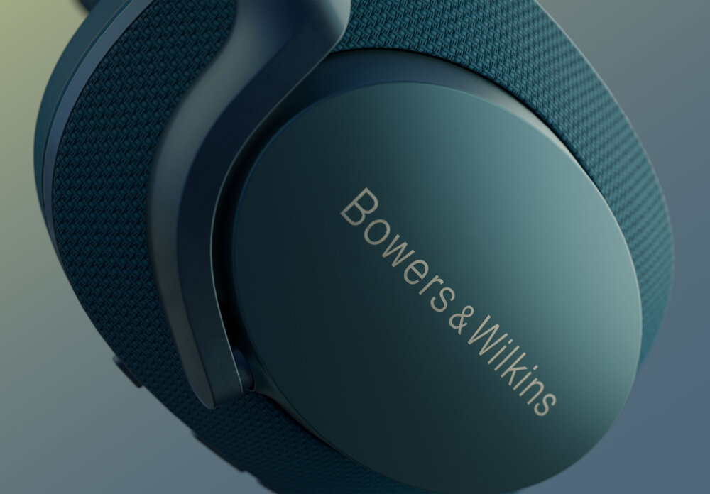 Zbliżenie na niebieskie słuchawki nauszne z widocznym napisem \'Bowers & Wilkins\' na nausznicy. Materiał na pałąku ma teksturę przypominającą tkaninę.