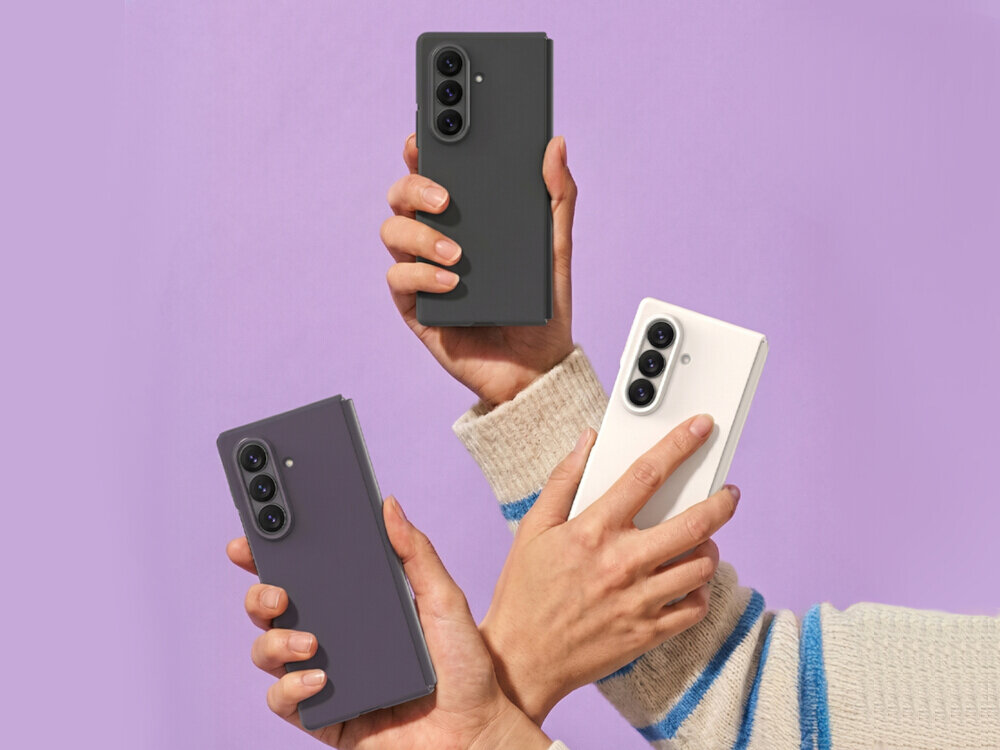 Trzy ręce trzymają smartfony w etui w różnych kolorach: czarnym, fioletowym i białym, na fioletowym tle. Każdy telefon ma widoczne trzy obiektywy aparatu z tyłu.