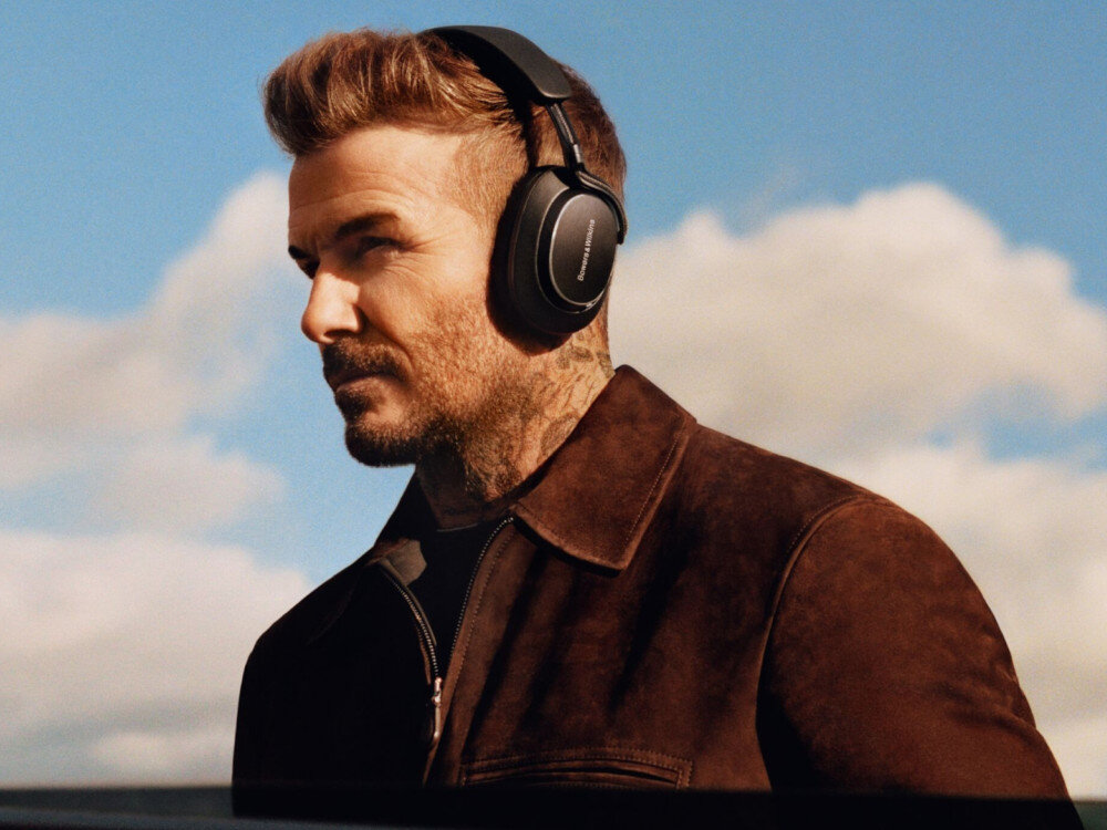Mężczyzna nosi czarne słuchawki nauszne z widocznym logo \'Bowers & Wilkins\'. W tle widać niebo z chmurami.