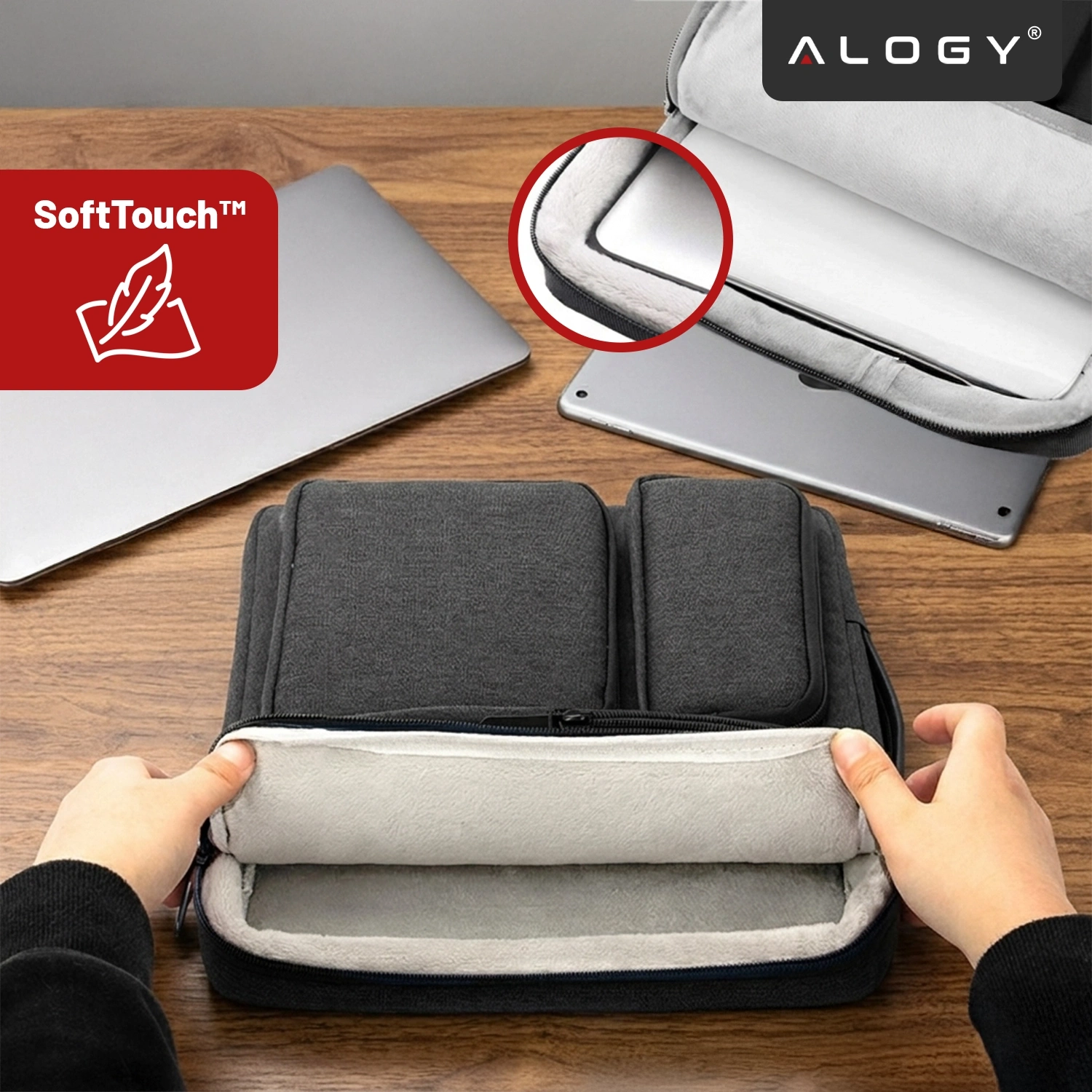 Na drewnianym stole leży czarna torba na laptopa z otwartą kieszenią, w której widać miękką, jasną wyściółkę. Obok znajduje się laptop, a w rogu widoczne jest logo \'ALOGY\' oraz czerwony znak z napisem \'SoftTouch™\'.