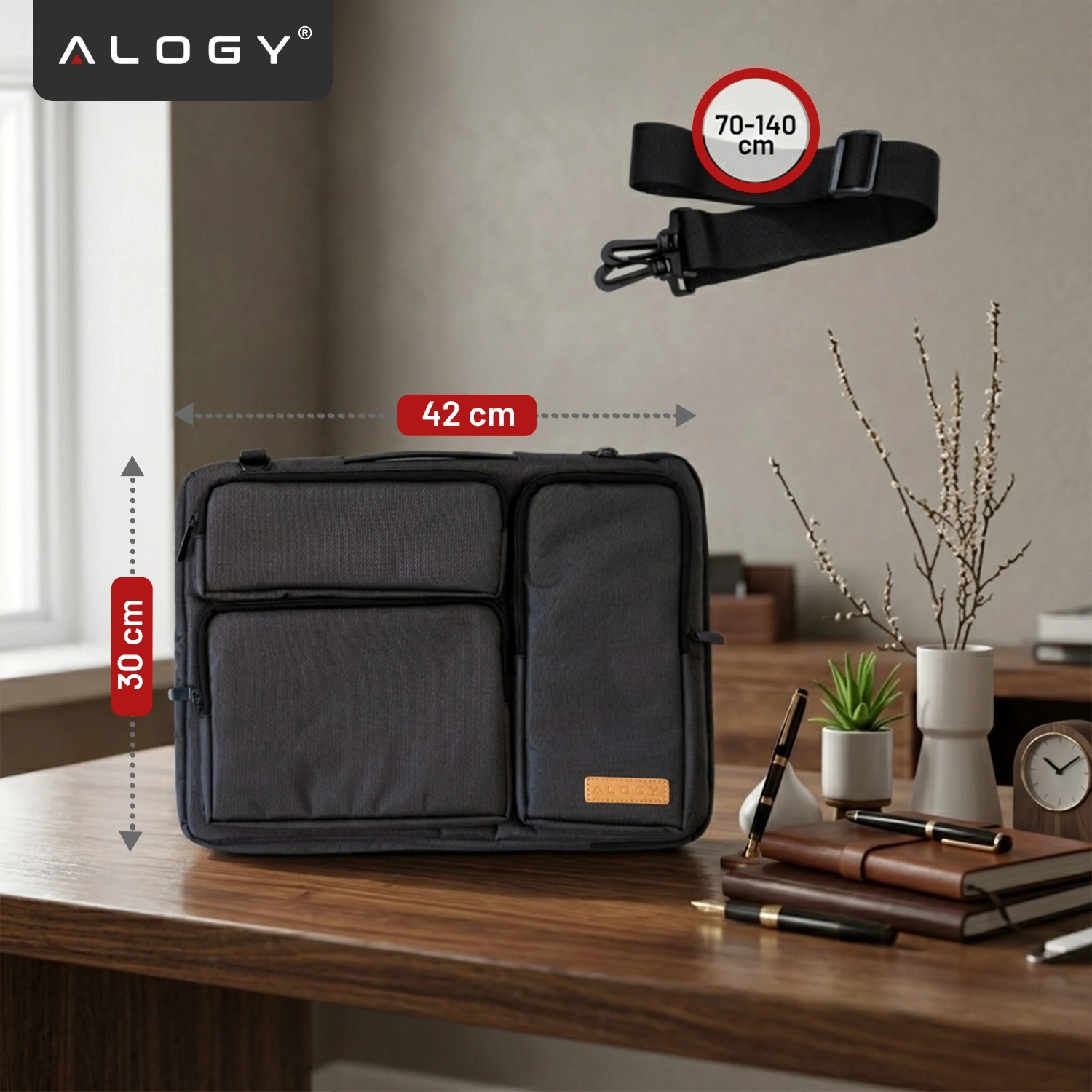 Czarna torba na laptopa z kilkoma kieszeniami, o wymiarach 42 cm na 30 cm, leży na drewnianym stole. Obok torby widoczny jest pasek na ramię o regulowanej długości 70-140 cm, a w tle znajdują się rośliny i przybory biurowe.