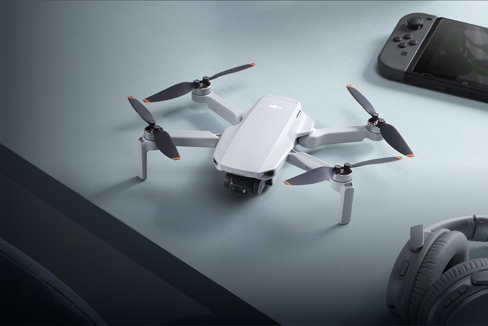 Na stole znajduje się biały dron z czterema śmigłami. Obok leżą słuchawki i urządzenie przypominające konsolę do gier.
