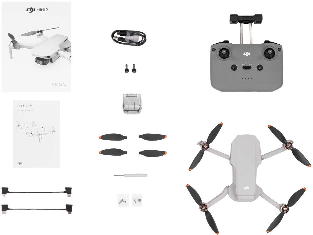 Na obrazie widoczny jest zestaw akcesoriów do drona DJI Mini 2, w tym dron, kontroler, śmigła, kabel, instrukcje oraz inne drobne elementy. Logo DJI jest widoczne na dronie i kontrolerze.