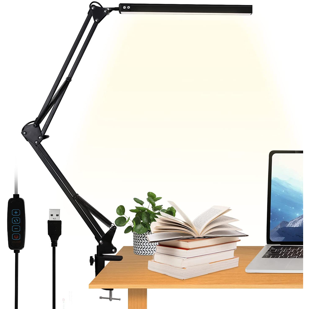 Czarna lampa biurkowa LED z regulowanym ramieniem zamocowana do blatu, obok stos książek, roślina w doniczce i laptop. Widoczny jest także przewód USB z panelem sterowania.