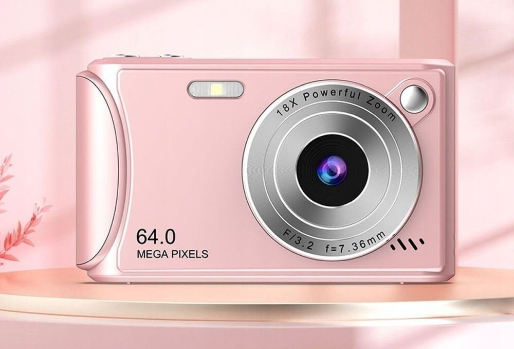 Różowy aparat fotograficzny z obiektywem oznaczonym jako \'18x Powerful Zoom\' i specyfikacją \'F/3.2 f=7.36mm\'. Na obudowie widnieje napis \'64.0 MEGA PIXELS\'.
