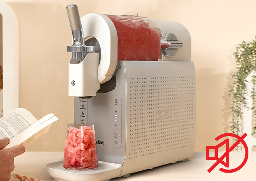 Maszynka do lodów z logo \'Tefal\' przygotowuje deser lodowy w szklance. Obok widoczna jest osoba trzymająca książkę.