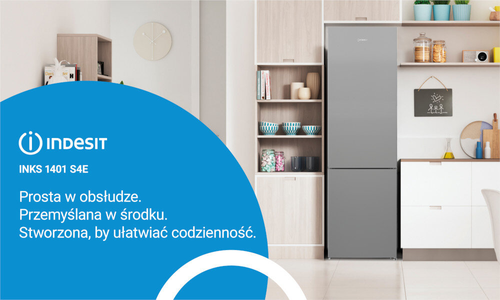 Obraz przedstawia srebrną lodówkę w zabudowie kuchennej z otwartymi półkami i szafkami. Po lewej stronie widoczny jest niebieski panel z logo \'INDESIT INKS 1401 S4E\' oraz tekstem: \'Prosta w obsłudze. Przemyślana w środku. Stworzona, by ułatwiać codzienność.\'