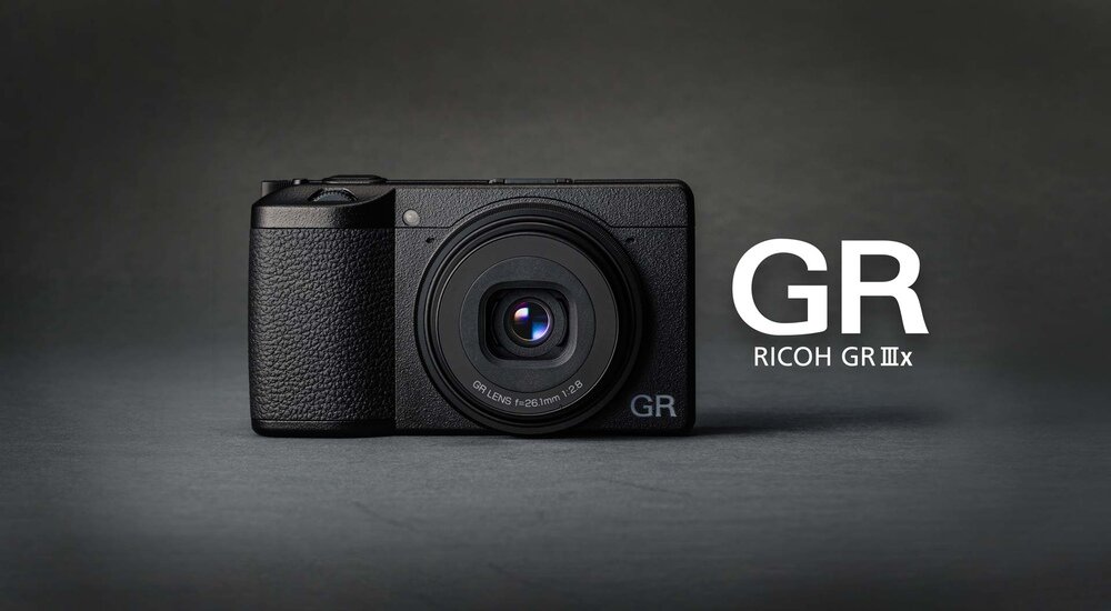 Czarny aparat fotograficzny z widocznym obiektywem i tekstem \'GR LENS f=40mm 1:2.8\' na pierścieniu. Obok aparatu znajduje się napis \'GR RICOH GR IIIx\'.
