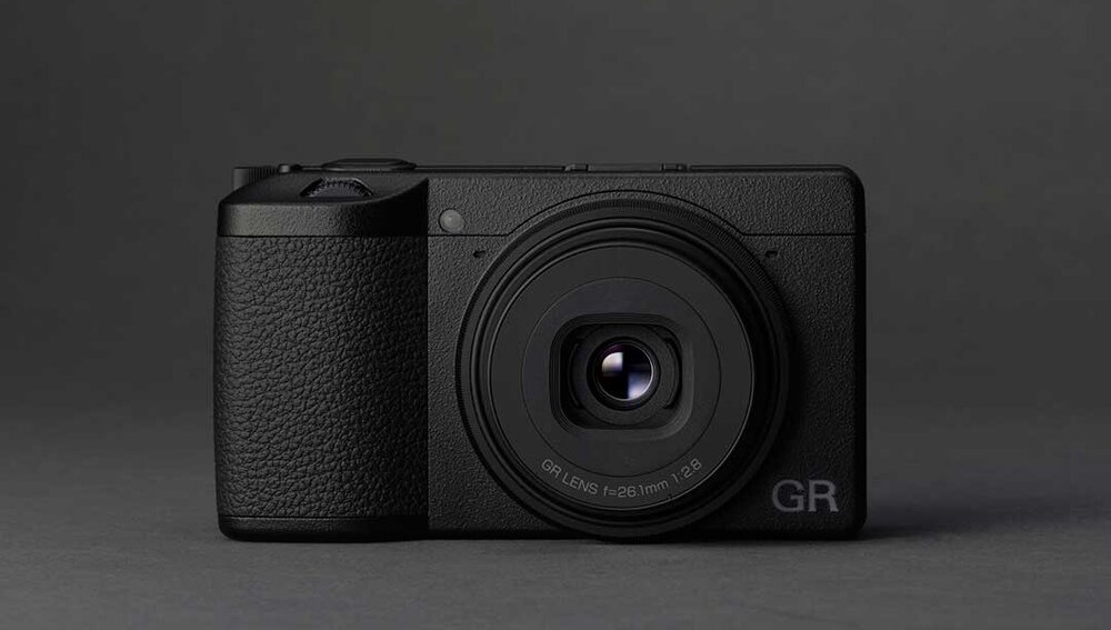 Czarny aparat fotograficzny z widocznym obiektywem i napisem \'GR LENS f=26.1mm 1:2.8\' na froncie. Na obudowie znajduje się logo \'GR\'.