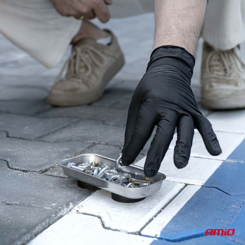 Osoba w czarnej rękawiczce trzyma metalową miskę magnetyczną z różnymi śrubami i nakrętkami. Na dole obrazu widoczne jest logo \'AMiO\'.