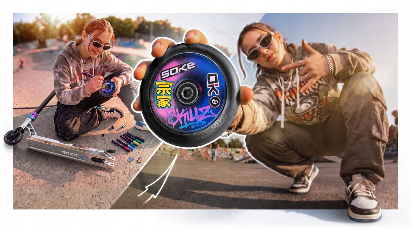 Osoba siedzi na ziemi obok srebrno-czarnej hulajnogi, trzymając w ręku koło z napisem \'SOKE\' oraz kolorowymi grafikami. W tle widać skatepark i kilka markerów leżących na ziemi.