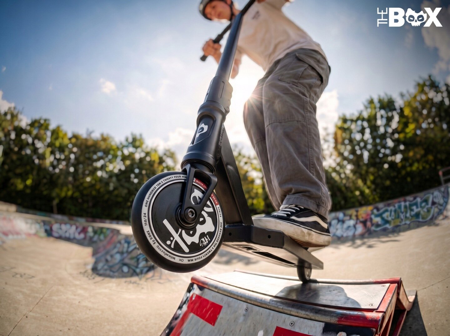 Osoba na hulajnodze wyczynowej wykonuje trik na rampie w skateparku. Na kole hulajnogi widoczny jest napis \'Hollow Core 110 mm\'.
