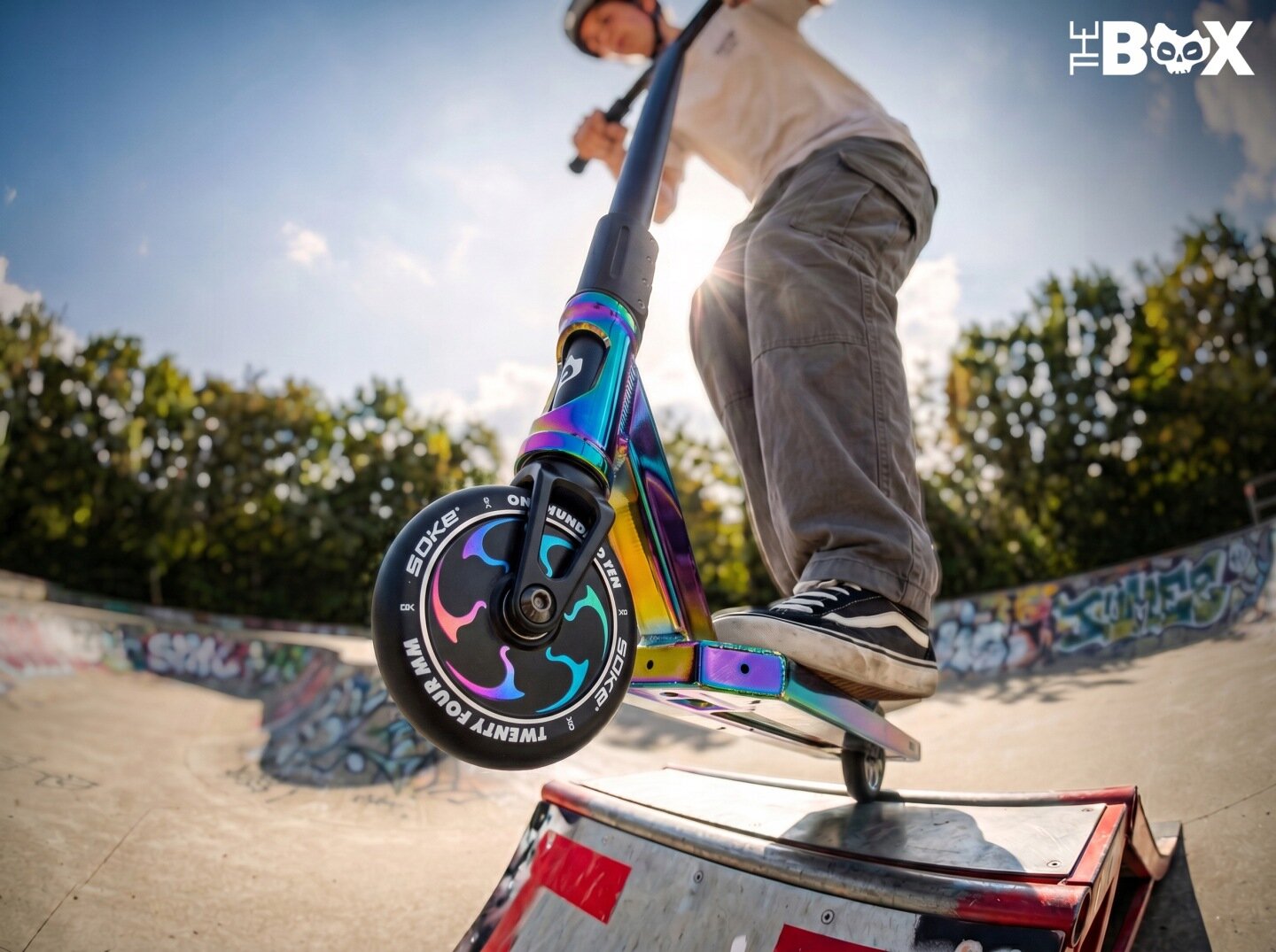 Osoba na hulajnodze wyczynowej wykonuje trik na rampie w skateparku. Na kole widoczny jest napis \'Soke\' oraz \'TWENTY FOUR MM\'.