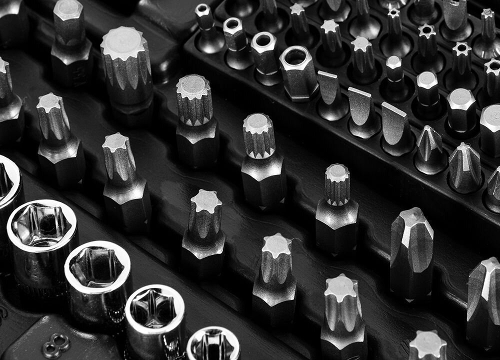 Zdjęcie przedstawia zestaw metalowych końcówek narzędziowych o różnych kształtach i rozmiarach, ułożonych w rzędach na ciemnym tle.