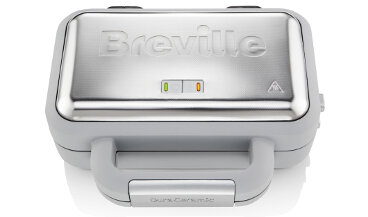 Na obrazie widoczna jest gofrownica z metaliczną pokrywą, na której znajduje się logo \'Breville\'. Obok logo znajdują się dwie kontrolki: zielona i pomarańczowa, a poniżej uchwyt z napisem \'DuraCeramic\'.