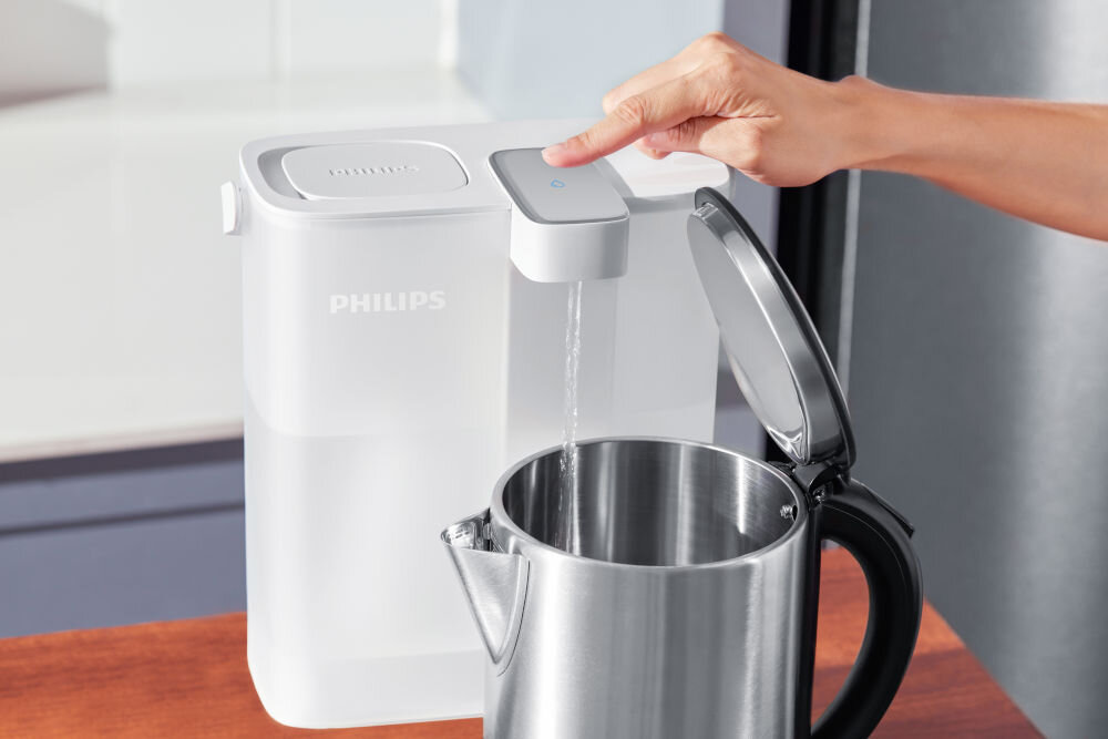 Dzbanek filtrujący PHILIPS z logo, z którego nalewana jest woda do metalowego czajnika. Osoba naciska przycisk na dzbanku.
