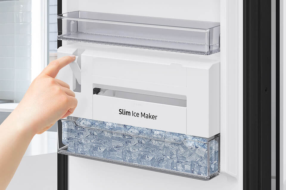 Szybka i wygodna kostkarka do lodu SLIM umieszczona na drzwiach zamrażarki RZ32C7CBEB1 Osoba obsługuje urządzenie do robienia lodu oznaczone jako \'Slim Ice Maker\', wypełnione kostkami lodu.