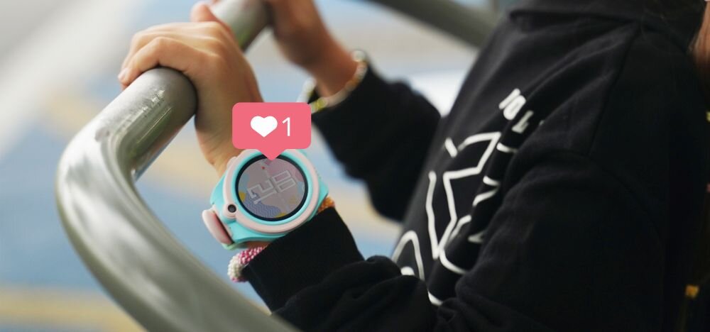 Osoba trzyma się poręczy, na nadgarstku ma różowy smartwatch z wyświetlaczem pokazującym godzinę 4:35. Nad zegarkiem widoczna jest ikona serca z liczbą 1.