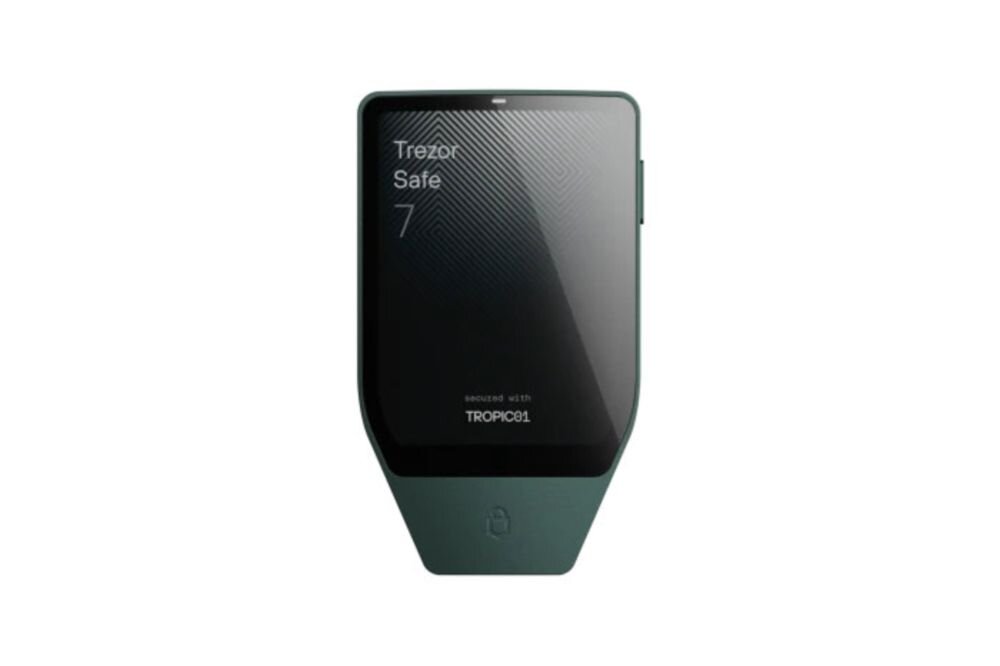 Na obrazie widoczny jest zielony portfel kryptowalut z wyświetlaczem, na którym znajduje się tekst: \'Trezor Safe 7 secured with TROPIC01\'.