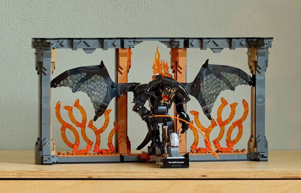 Model LEGO przedstawiający scenę z Balrogiem, z płomieniami i skrzydłami, umieszczony na półce. Na podstawce widnieje napis: \'You shall not pass!\'.