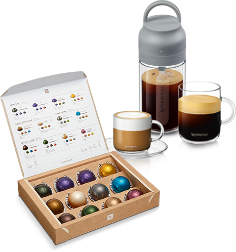 Na obrazie znajduje się otwarte pudełko z kapsułkami Nespresso w różnych kolorach oraz trzy filiżanki z kawą, z czego jedna jest przezroczysta z logo Nespresso. Obok znajduje się szary pojemnik z uchwytem, również z logo Nespresso.