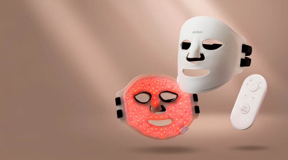 Na obrazie widoczne są dwie maski LED do twarzy oraz pilot zdalnego sterowania. Jedna z masek świeci czerwonym światłem, a na drugiej widnieje logo \'cecotec\'.
