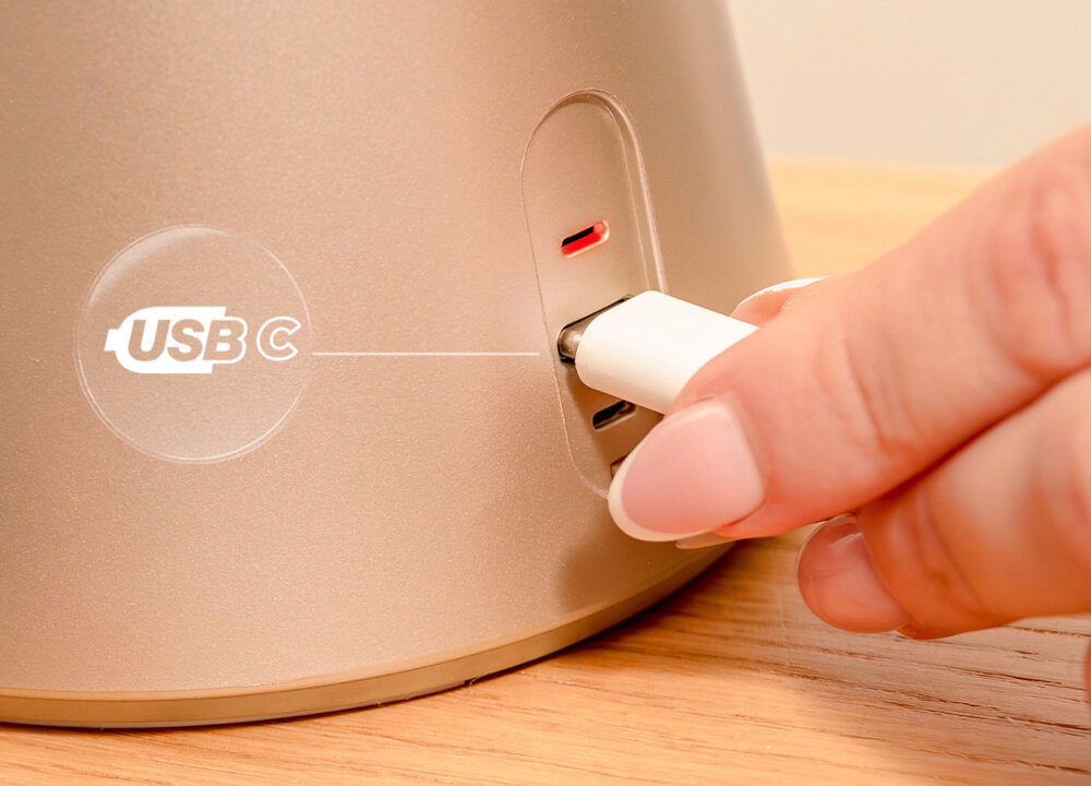 Osoba podłącza kabel USB-C do portu w urządzeniu o złotym kolorze. Obok portu widoczny jest symbol \'USB C\'.
