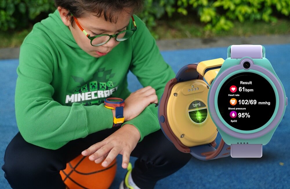Dziecko w zielonej bluzie siedzi na niebieskiej powierzchni z pomarańczową piłką, nosząc smartwatch na nadgarstku. Obok widoczny jest zbliżony obraz smartwatcha z wyświetlaczem pokazującym wyniki: Heart rate 61 bpm, Blood pressure 102/69 mmhg, SpO2 95%.