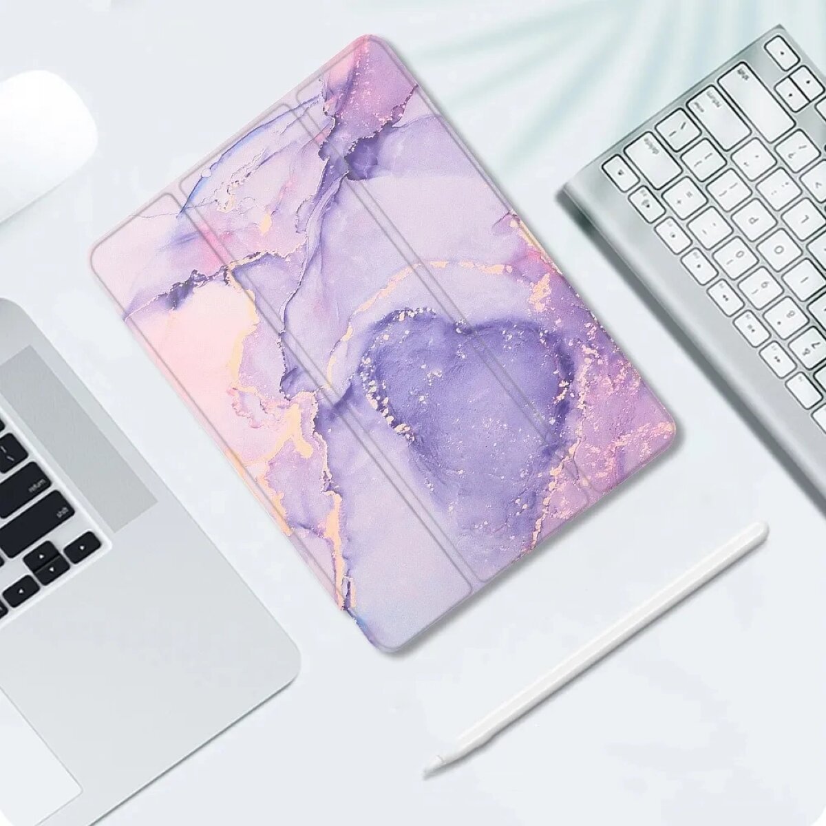 Na obrazie widoczne jest etui z abstrakcyjnym wzorem w odcieniach fioletu i różu, leżące obok klawiatury i laptopa. Obok etui znajduje się biały rysik.