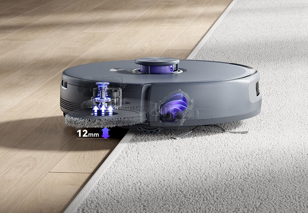 Robot sprzątający w kolorze szarym przejeżdża z twardej podłogi na dywan, z widocznym mechanizmem podnoszenia o 12 mm. Obok robota znajdują się graficzne elementy wskazujące na jego funkcje technologiczne.