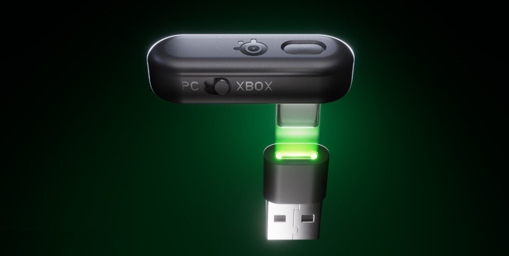 Na obrazie widoczny jest czarny adapter USB z logo producenta i przełącznikiem oznaczonym jako \'PC\' i \'XBOX\'. Adapter jest podświetlony na zielono, a w tle widoczny jest ciemnozielony gradient.