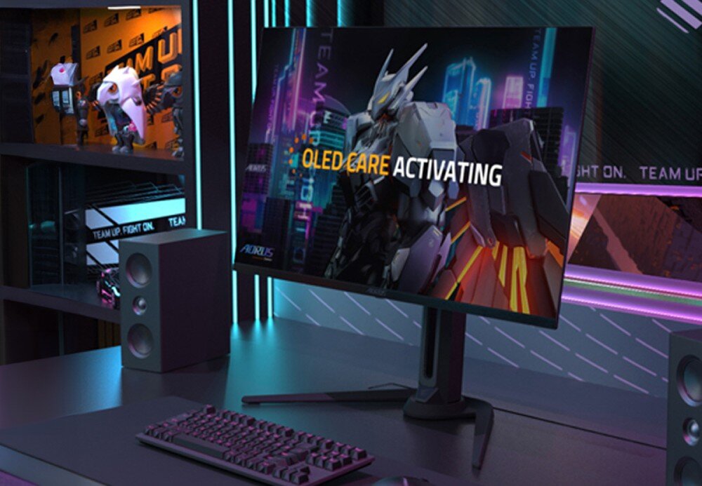 Na biurku znajduje się monitor z wyświetlonym obrazem robota i tekstem \'OLED CARE ACTIVATING\'. W tle widoczne są półki z figurkami i neonowe oświetlenie.