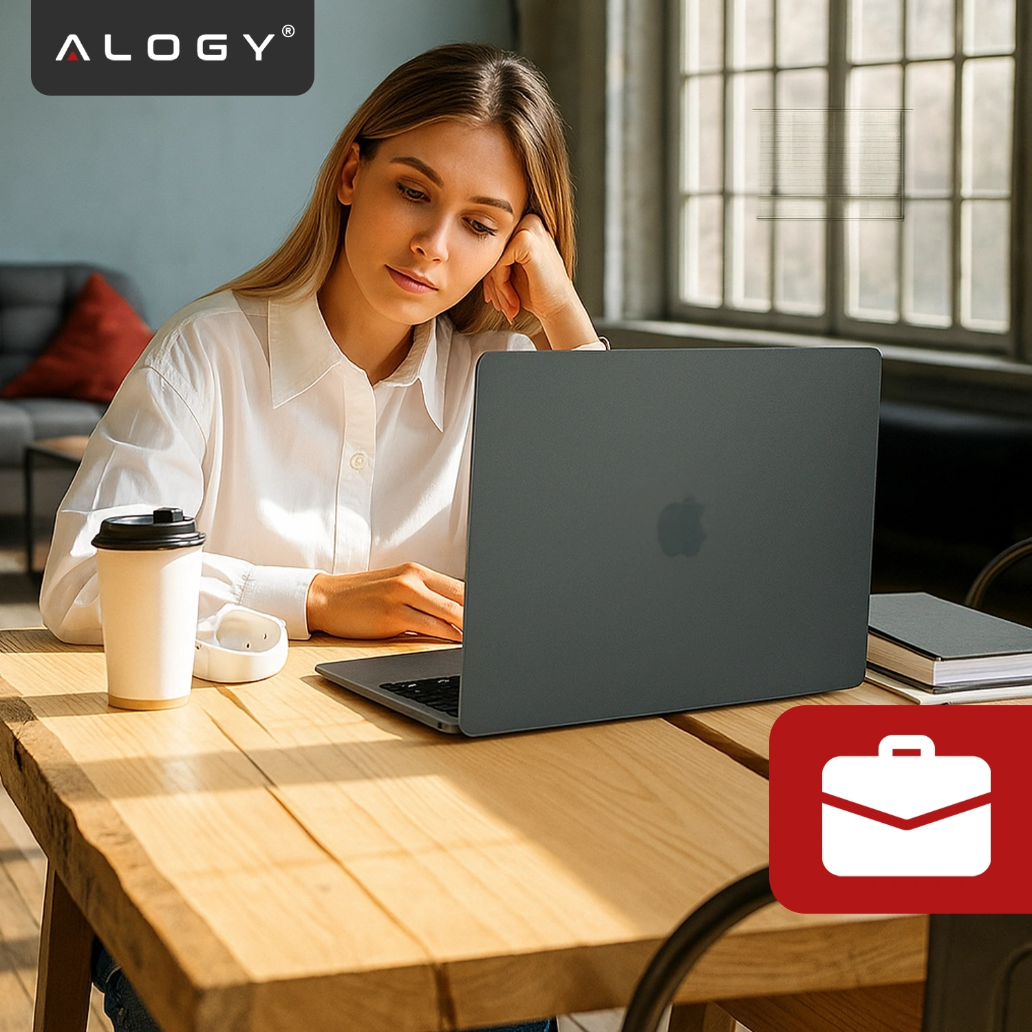 Kobieta siedzi przy drewnianym stole, używając laptopa z czarnym, matowym etui. W lewym górnym rogu widoczne jest logo \'ALOGY\'.