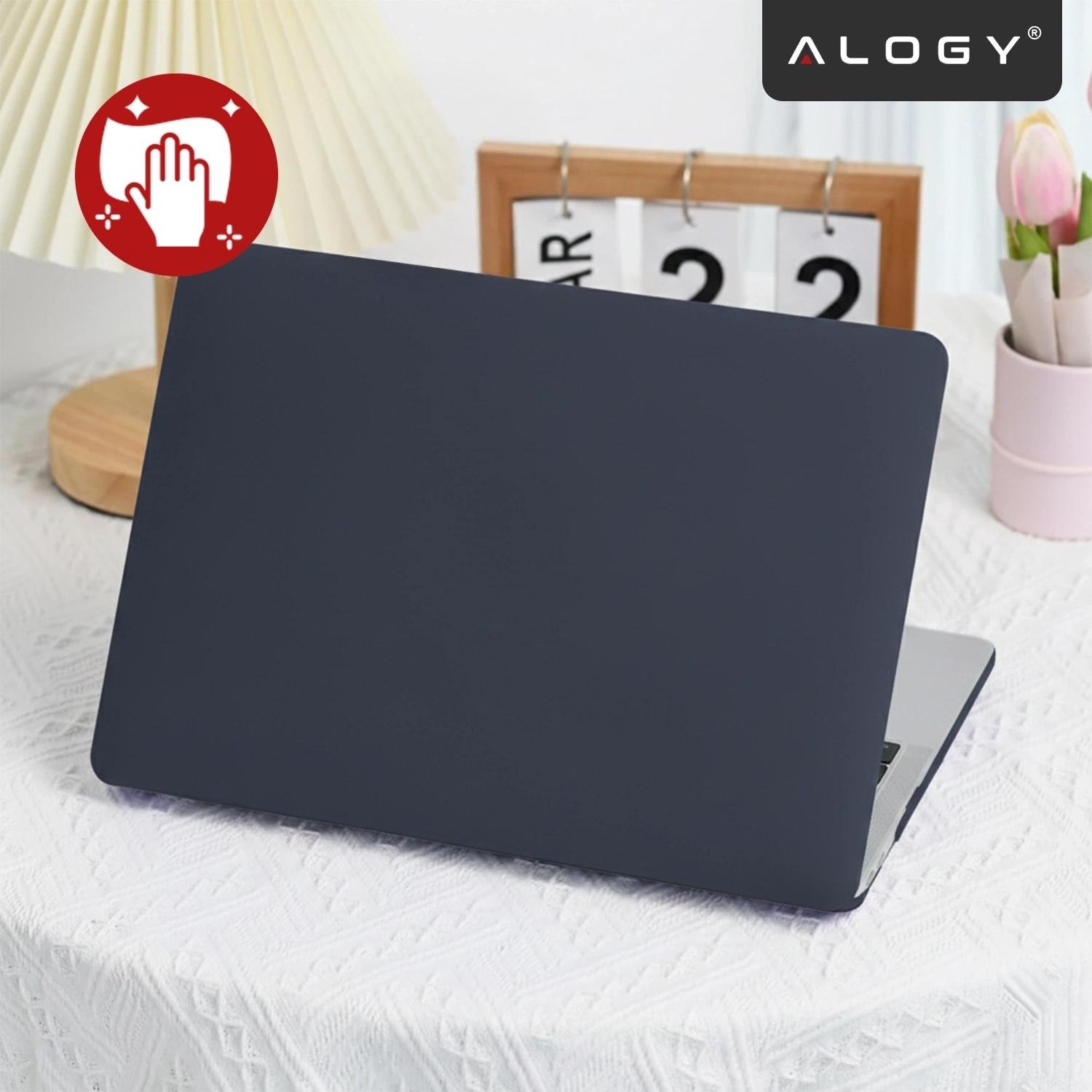 Na stole znajduje się laptop z granatowym etui, obok stoi lampa i kalendarz z datą 22. W prawym górnym rogu widoczne jest logo \'ALOGY\'.