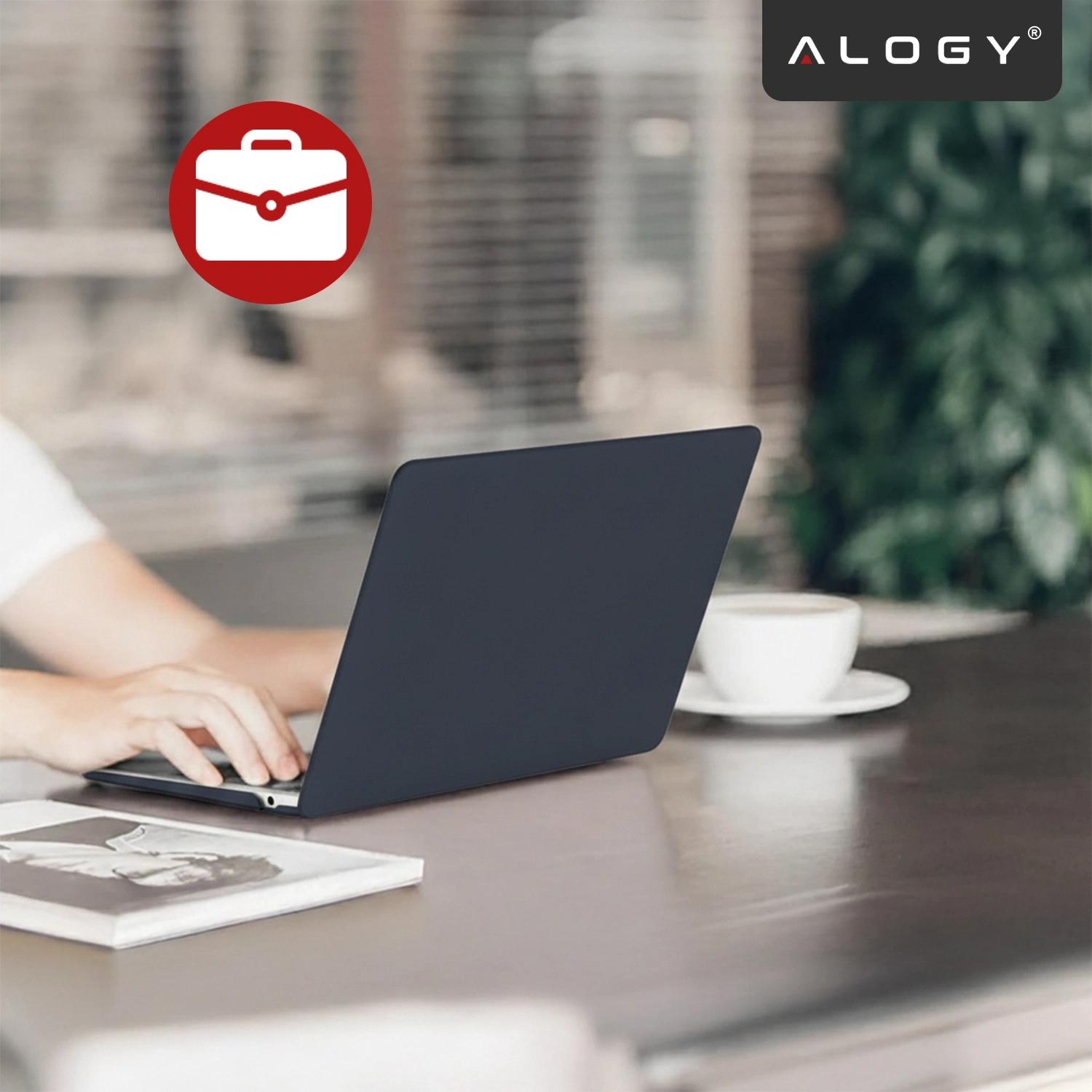 Osoba korzysta z laptopa z granatowym etui na biurku, obok znajduje się filiżanka kawy. W prawym górnym rogu widoczne jest logo \'ALOGY\'.
