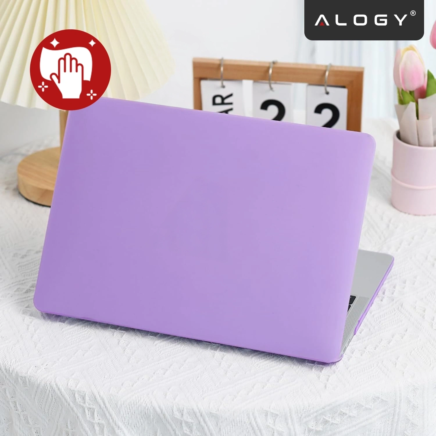 Na obrazie widoczny jest laptop w fioletowym, matowym etui, stojący na białym obrusie. W tle znajduje się kalendarz, lampka oraz kwiaty, a w prawym górnym rogu widnieje logo \'ALOGY\'.