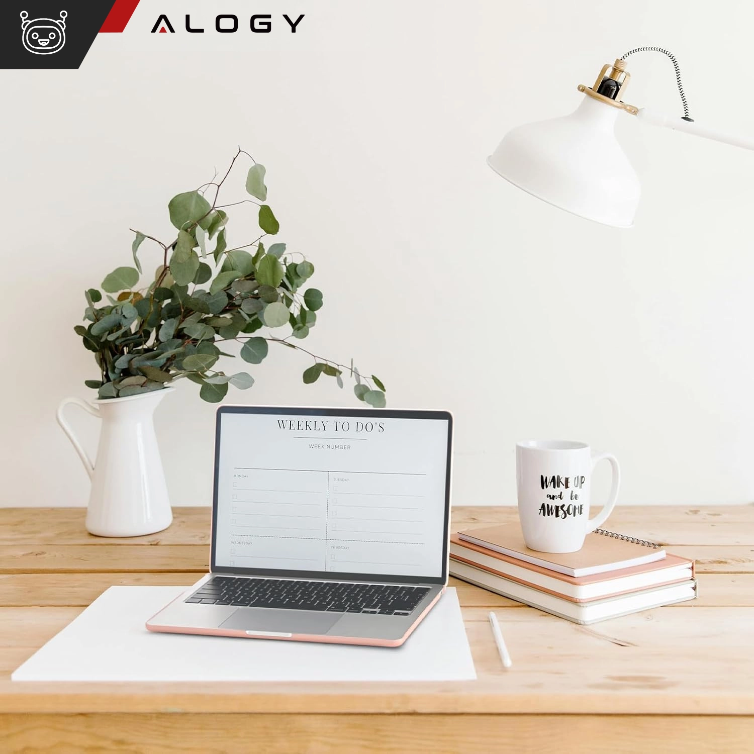 Na drewnianym stole stoi otwarty laptop z widocznym ekranem z napisem \'WEEKLY TO DO\'S\'. Obok znajduje się kubek z napisem \'WAKE UP and BE AWESOME\', kilka zeszytów oraz biała lampa i wazon z zielonymi gałązkami.